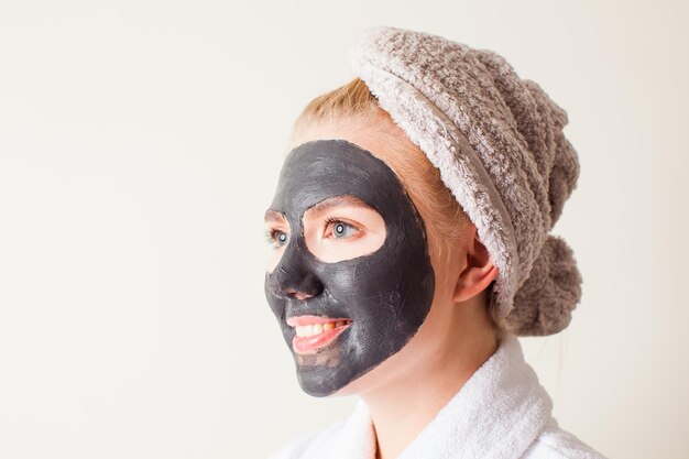 Beautiful young woman using a black face mask, close up. Spa treatment