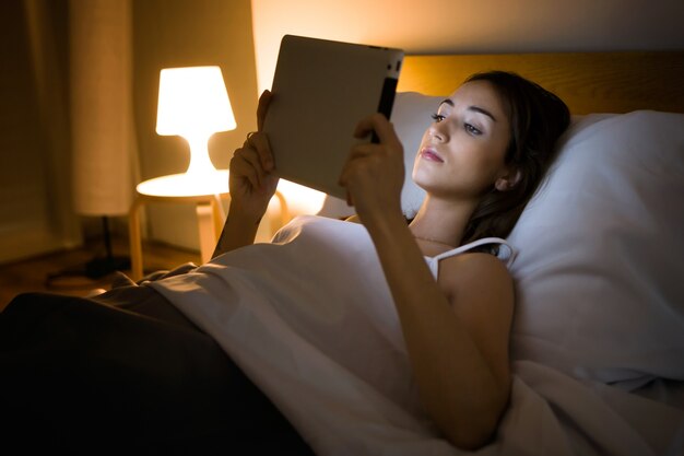 Foto bella giovane donna che utilizza la sua compressa digitale nel letto di notte.