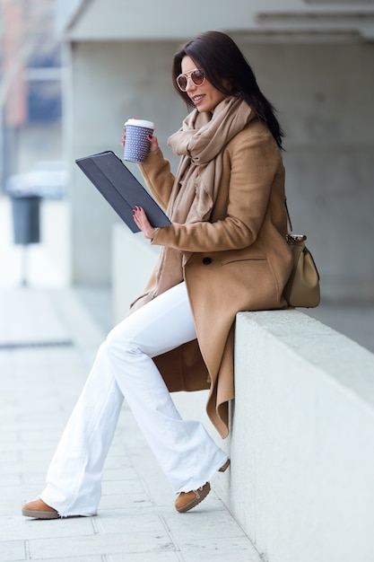 彼女のデジタルタブレットを通りで使っている美しい若い女性。