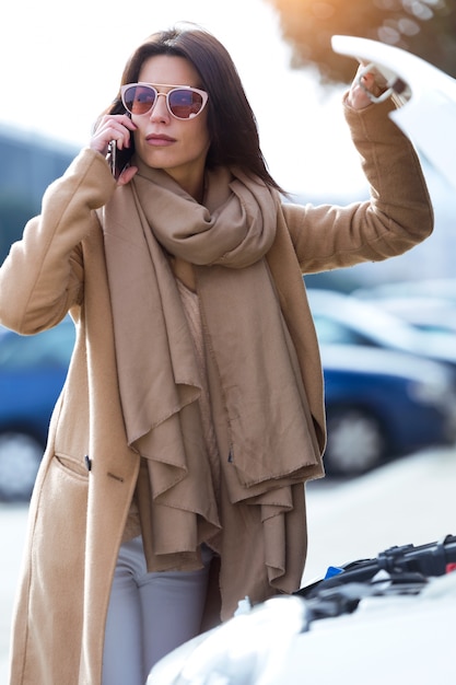Foto la bella giovane donna che usando il suo telefono cellulare richiede assistenza per l'automobile