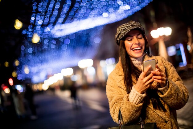 クリスマスの時期に路上で彼女の携帯電話を使用して美しい若い女性