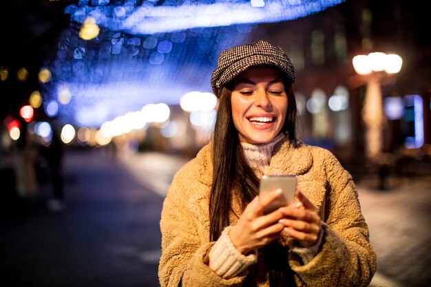 クリスマスの時期に路上で彼女の携帯電話を使用して美しい若い女性