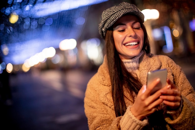 クリスマスの時期に路上で彼女の携帯電話を使用して美しい若い女性