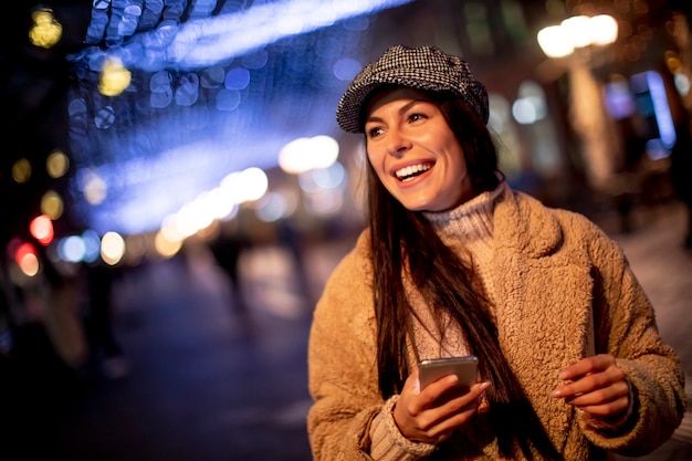 クリスマスの時期に路上で彼女の携帯電話を使用して美しい若い女性