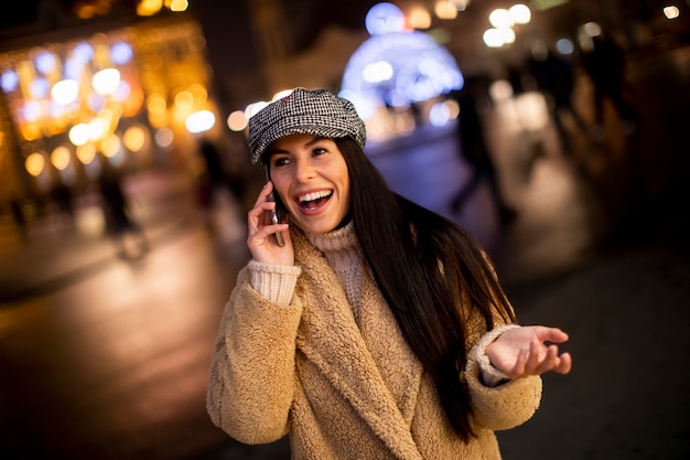 Beautiful young woman using her mobile phone in the street at Christmas time