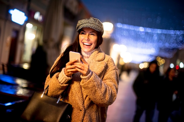 Bella giovane donna che usa il suo telefono cellulare in strada a natale