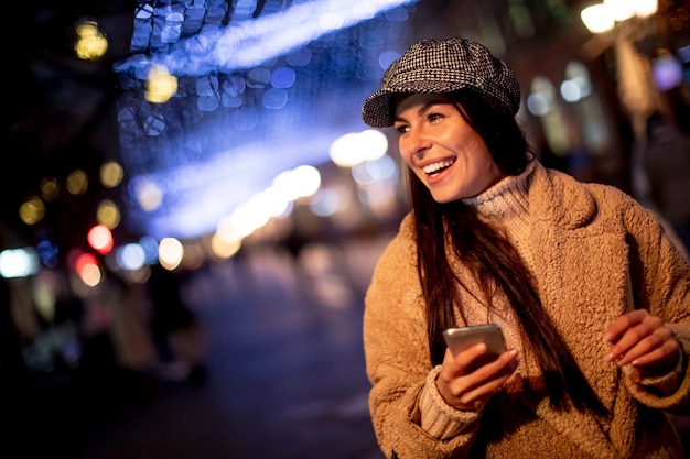 クリスマスの時期に路上で彼女の携帯電話を使用して美しい若い女性