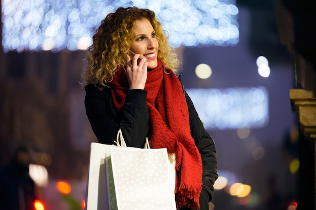 Foto bella giovane donna usando il suo telefono cellulare in strada di notte.