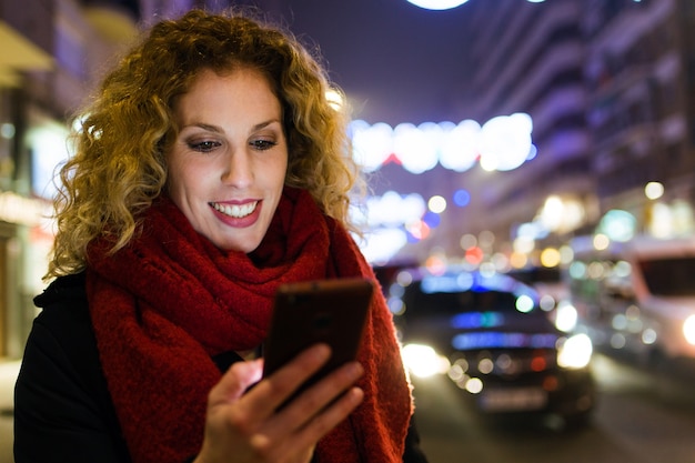 Foto bella giovane donna usando il suo telefono cellulare in strada di notte.