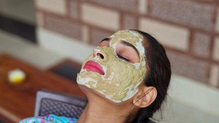 Beautiful young woman using homemade facial mask on face and relaxing at home multani mitti