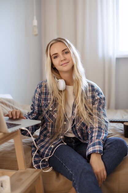 Beautiful young woman using a laptop computer while sitting on the bed at home. Cute girl in