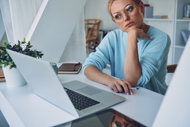 Beautiful young woman using laptop and looking thoughtful while working in office