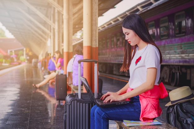 美しい若い女性は、列車の駅で待っている間にラップトップを使用しています。