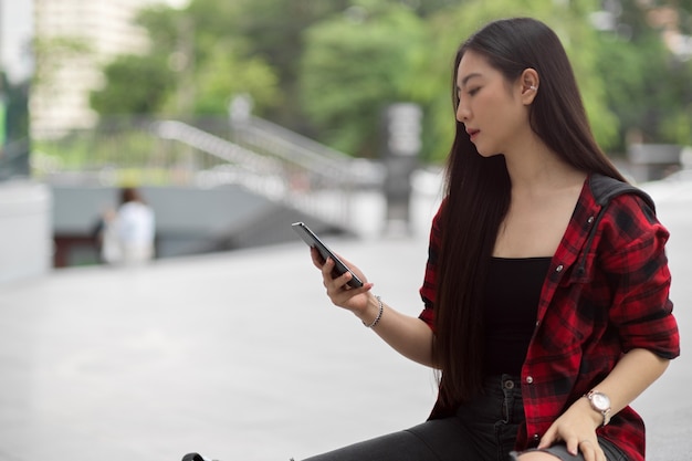 Beautiful young woman using smartphone in city street, holding mobile phone