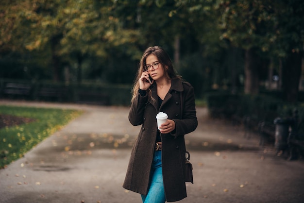 スマートフォンを使用してコーヒーの持ち帰りを飲む美しい若い女性