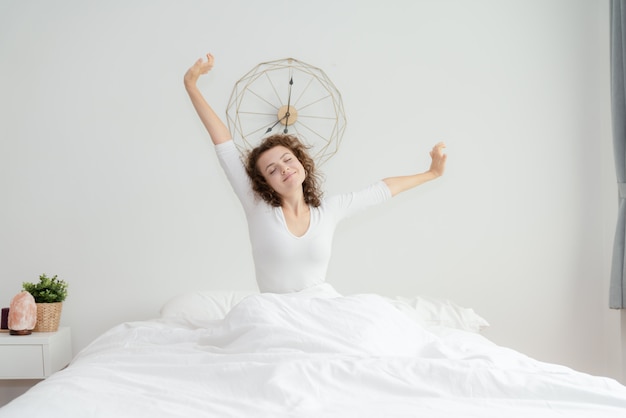 Beautiful young woman waking up and stretching in her bed in the morning