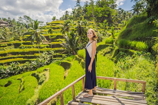 Beautiful young woman walk at typical Asian hillside with rice farming mountain shape green cascade rice field terraces paddies Ubud Bali Indonesia Bali travel concept