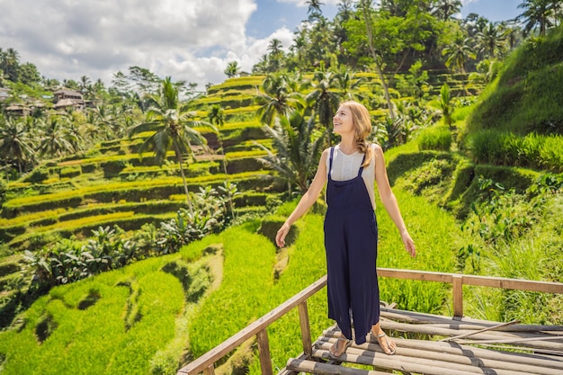 Beautiful young woman walk at typical Asian hillside with rice farming mountain shape green cascade rice field terraces paddies Ubud Bali Indonesia Bali travel concept