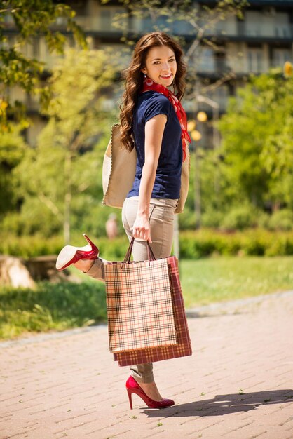 Красивая молодая женщина гуляет в парке и держит сумки с покупками.