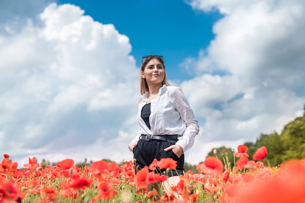 Bella giovane donna che cammina nel campo di papaveri in una giornata estiva