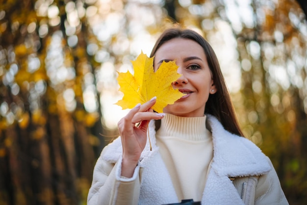 美しい若い女性が秋の公園を歩き手に黄色いメープルの葉を握っています 美しい若き女性が秋的公園を歩い手に 黄色いメイプルの葉が握っています