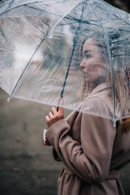 Фото Красивая молодая женщина гуляет в осеннем парке с ярким прозрачным зонтиком осеннее настроение