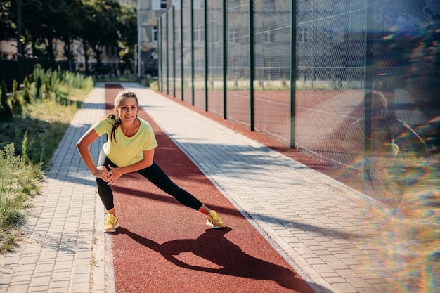 Beautiful young woman warming up on red track before run