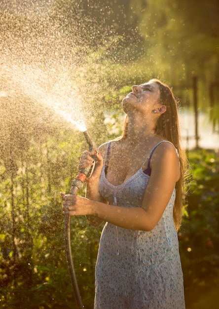 Beautiful young woman watering garden with hose pipe