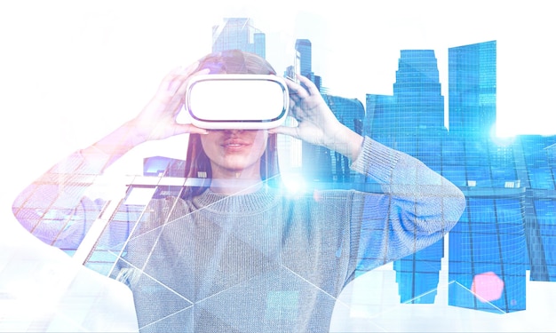beautiful young woman wearing beige sweater and vr glasses standing over blue cityscape background. toned image double exposure