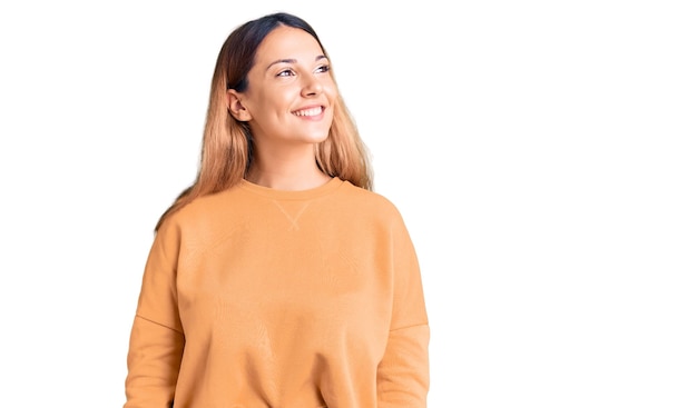 Beautiful young woman wearing casual clothes looking away to side with smile on face, natural expression. laughing confident.