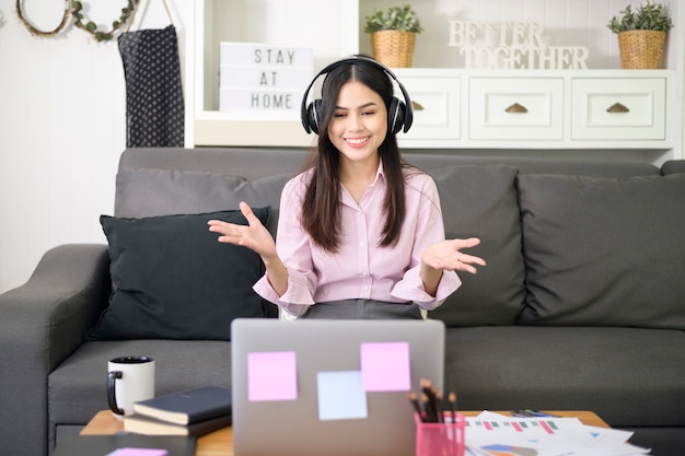 Una bella giovane donna che indossa l'auricolare sta effettuando una videoconferenza tramite computer a casa, concetto di tecnologia aziendale.