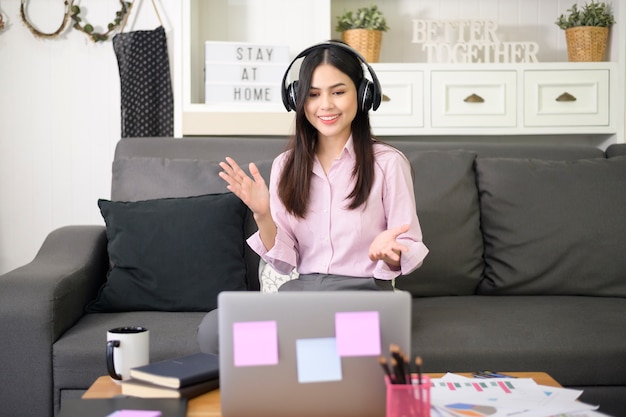 Una bella giovane donna che indossa l'auricolare sta effettuando una videoconferenza tramite computer a casa, concetto di tecnologia aziendale.
