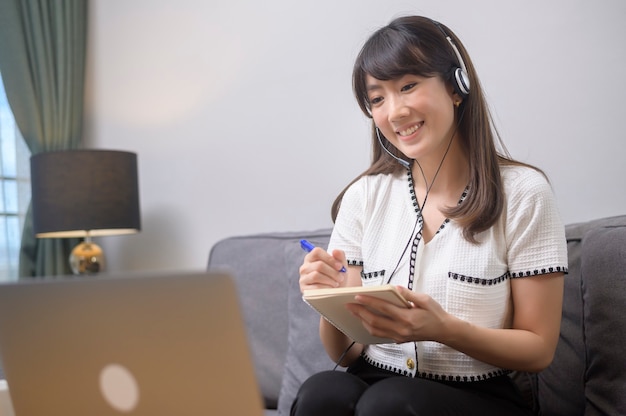 A beautiful young woman wearing headset is making video conference call via computer at home