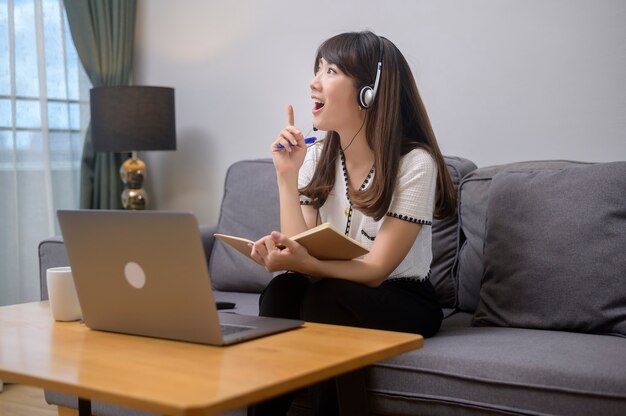 A beautiful young woman wearing headset is making video conference call via computer at home