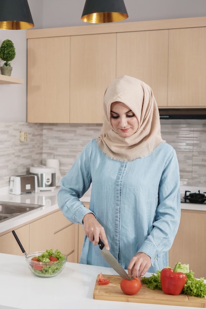 Beautiful young woman wearing hijab preparing vegetable salad