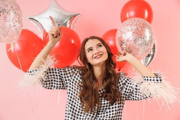 Bella giovane donna che indossa una giacca in piedi isolato su sfondo rosa, celebrando, tenendo un mazzo di palloncini