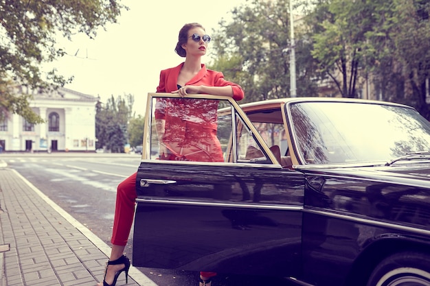 Foto bella giovane donna che indossa il costume rosso mentre si trovava vicino a un'auto retrò