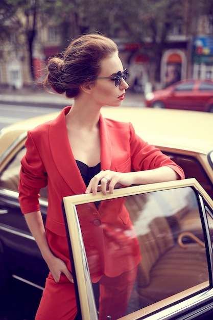 레트로 자동차 근처에 서있는 동안 빨간색 의상을 입고 아름 다운 젊은 여자