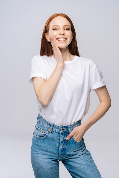 完璧な滑らかな顔の肌に触れるTシャツとデニムパンツを着ている美しい若い女性