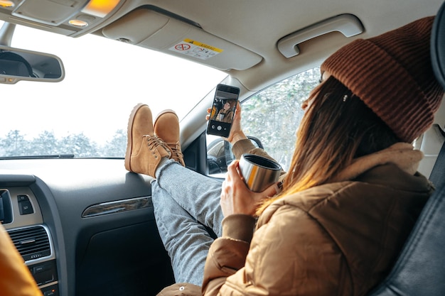 Beautiful young woman wearing warm clothes sitting in car while winter road trip