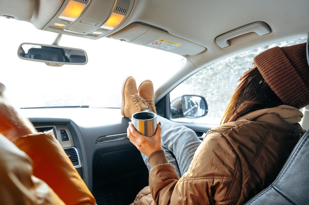 Beautiful young woman wearing warm clothes sitting in car while winter road trip