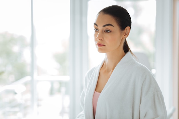 Beautiful young woman wearing a white robe while getting ready to a procedure in the beauty salon