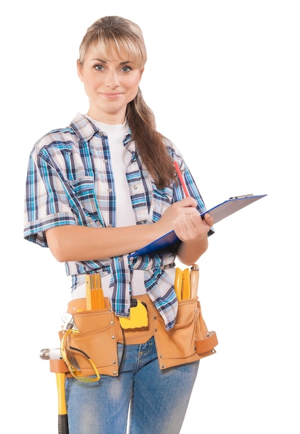 Beautiful young woman wearing working clothes holding clipboard pencil with some tools standing looking at camera