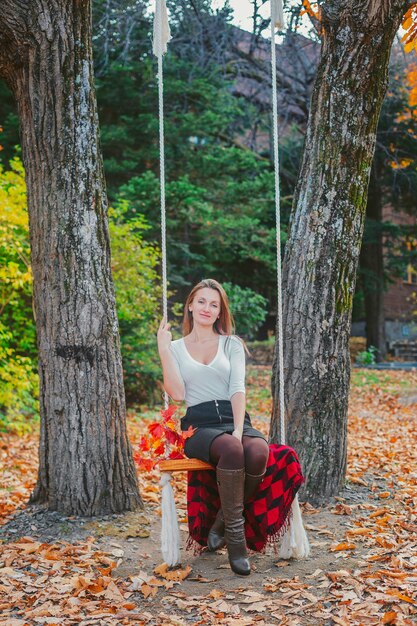 Beautiful young woman in a white blouse in the park in autumn. Young woman in the park sitting on a swing