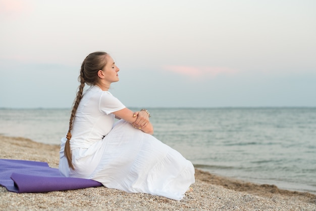 Beautiful young woman in white clothes sitting on sandy beach and enjoy silence