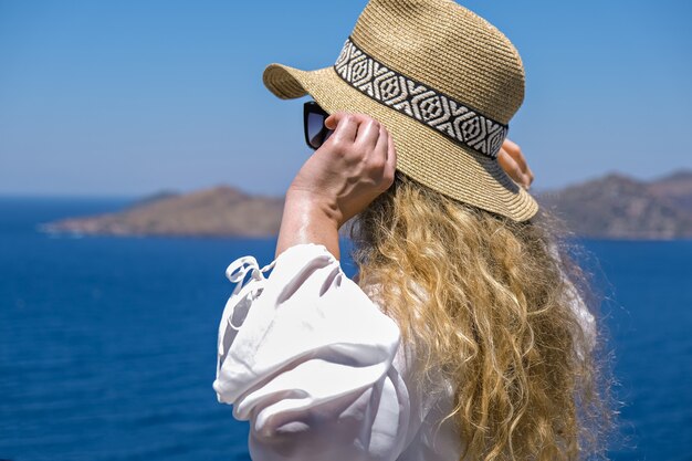 Beautiful young woman in white dress sunglasses and bikini straw hat looking at sea