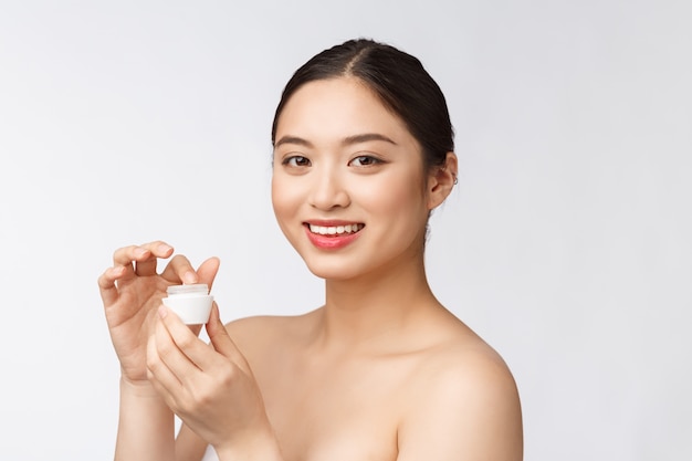 Beautiful young woman on white isolated wall holding cosmetic face cream, asian