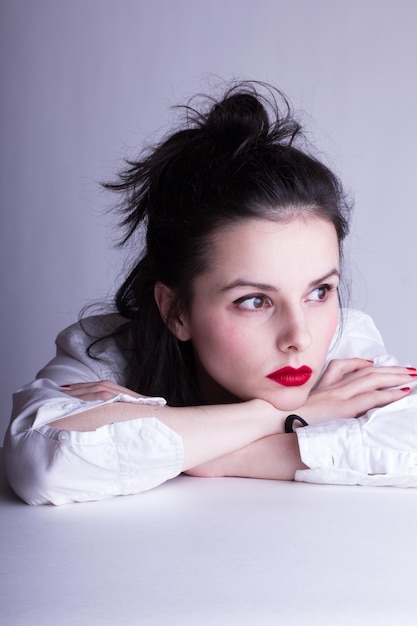 beautiful young woman in a white shirt on a white background with red lipstick on her lips