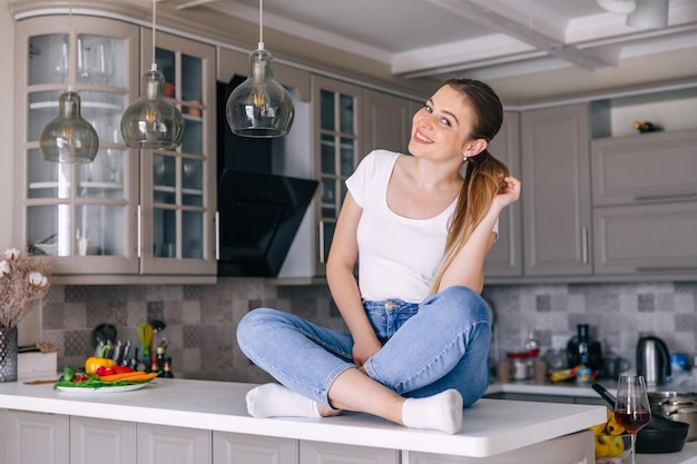 Beautiful young woman in white tshirt and jeans sitting in the kitchen