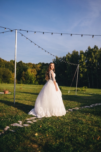 Bella giovane donna in un abito da sposa bianco e stivali neri al tramonto.